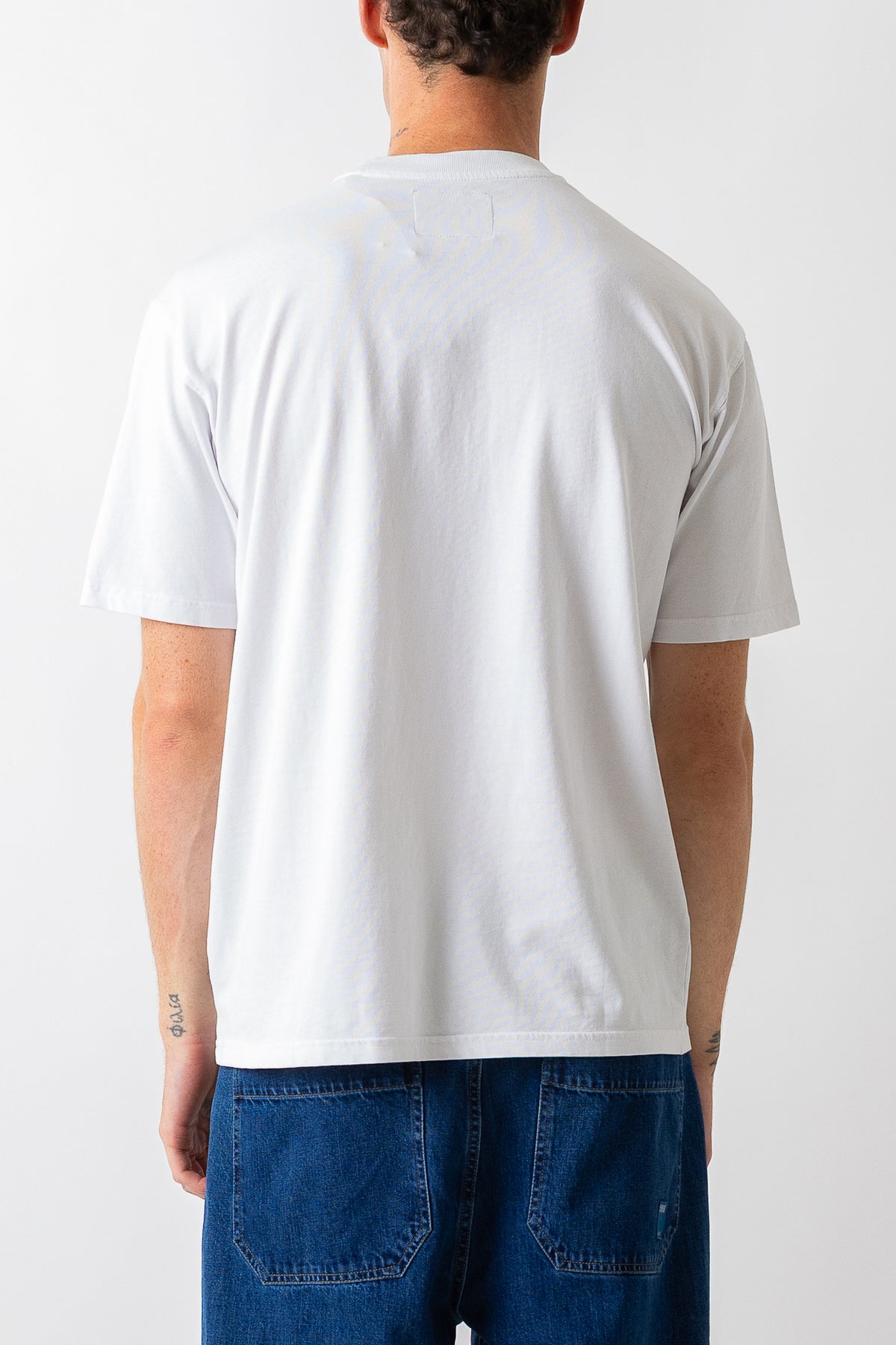 A man viewed from behind wearing a plain white short-sleeve t-shirt and blue jeans against a clean white background.