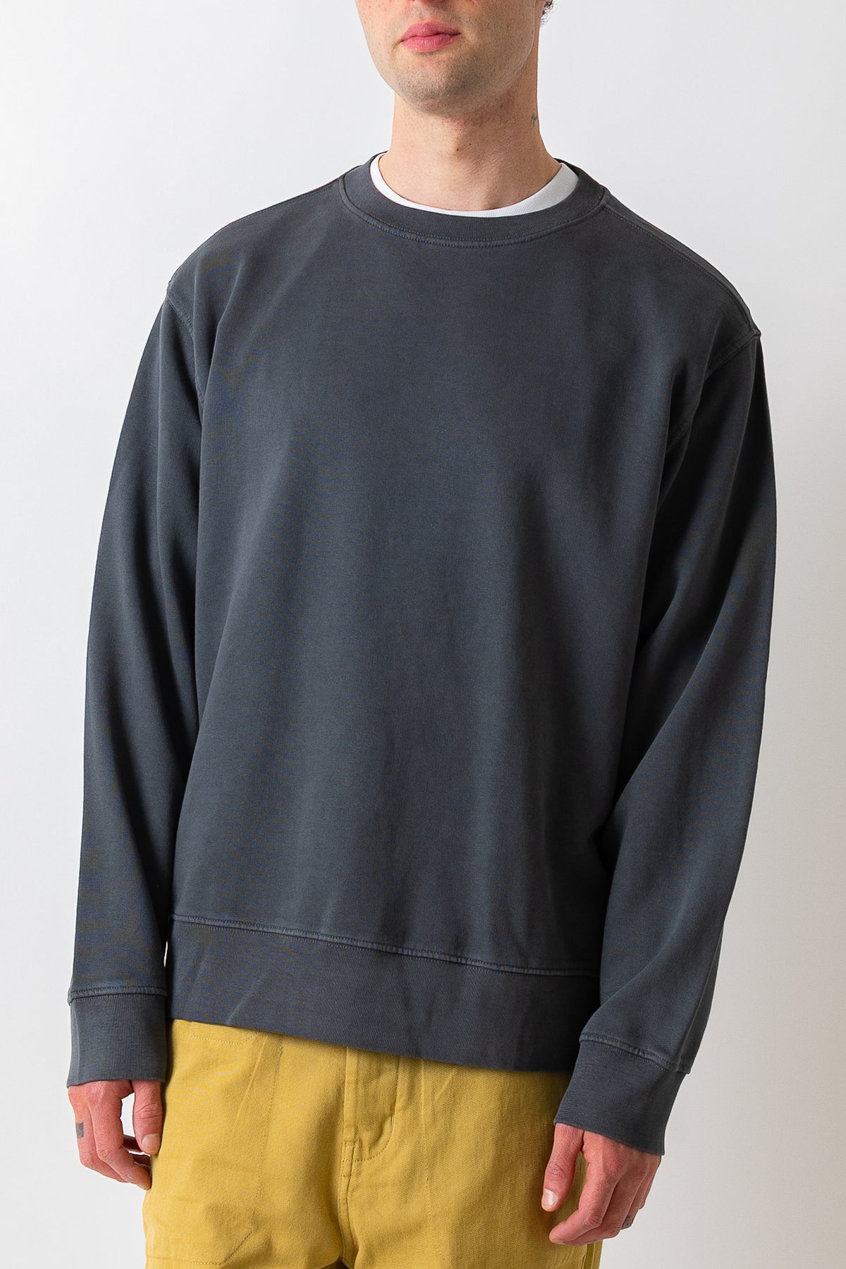 A man wearing a dark charcoal gray crewneck sweatshirt and mustard yellow pants, shown from the chin down against a plain light background.