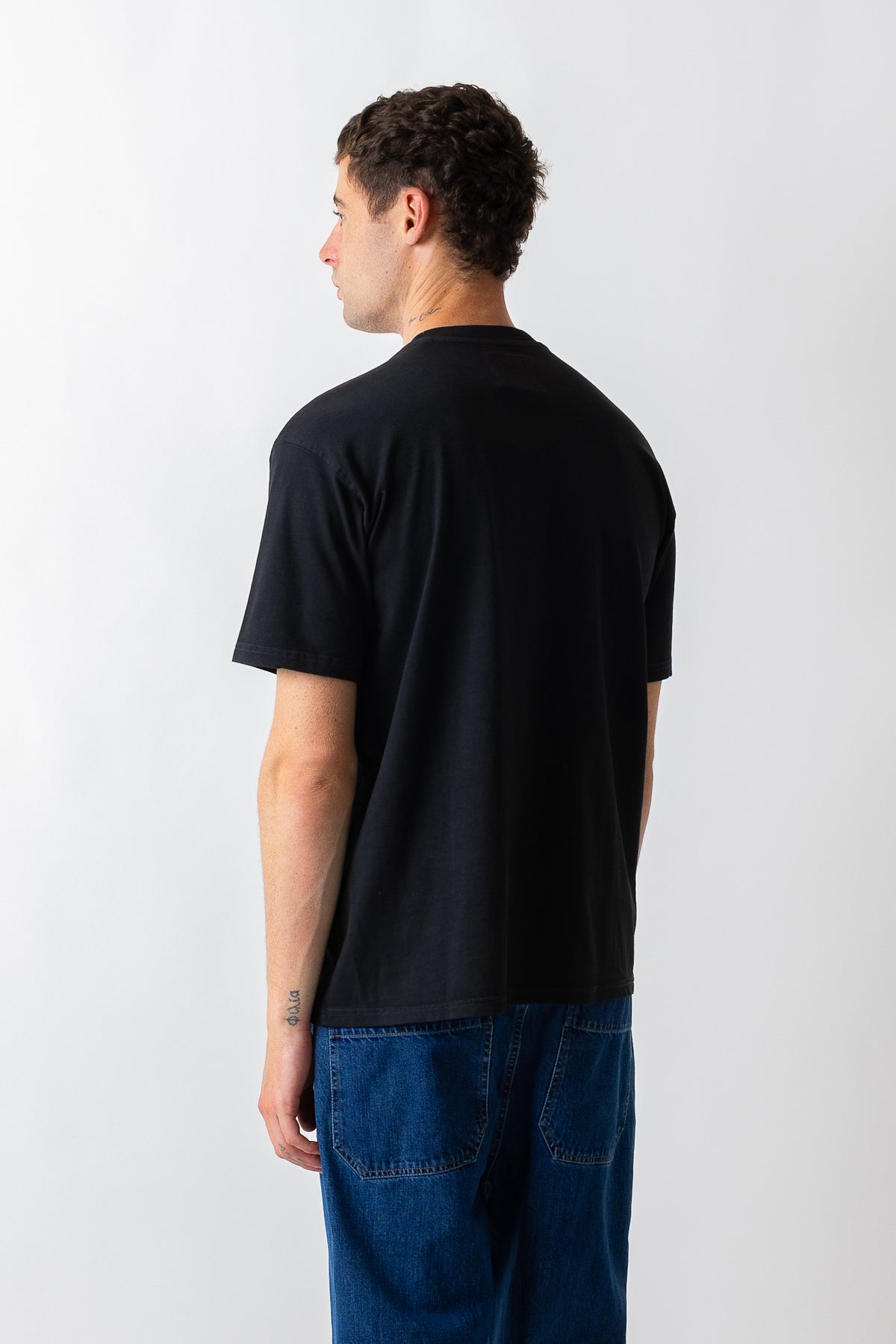 A man wearing a plain black short-sleeve t-shirt and blue jeans, shown from the back against a light gray studio background.